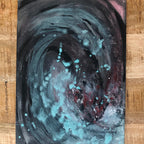 An abstract emotional drawing canvas art print painting of a swirling cosmic vortex with teal, black, and red tones, displayed on a light wood background.