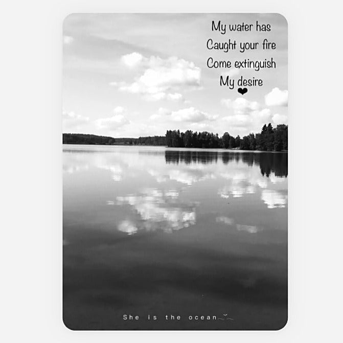 A rectangular Desire greeting card black and white art print featuring a serene lake reflection scene with clouds and trees, overlaid with the quote, 'My water has Caught your fire Come extinguish My desire' near the top and 'She is the ocean' at the bottom.