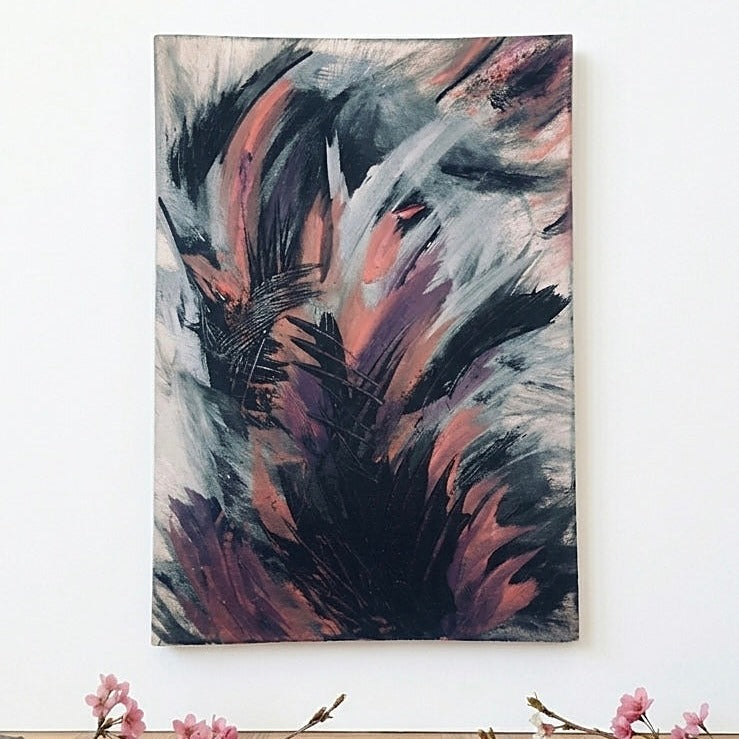 Abstract emotional canvas wall art print featuring expressive brushstrokes in black, gray, white, and dusty pink, hanging on a white wall above a surface with small pink blossoms at the bottom.