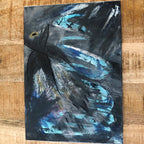 An abstract emotional canvas art print mixed-media painting featuring expressive brushstrokes in black, gray, and vibrant blue, with a small yellow accent near the upper left, displayed on a wooden surface.