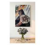 A vertical canvas artwork wall art print showing a close-up of a tattooed hand holding a large gray rose, displayed above a bouquet of gray roses on a light wood floor against a white wall.