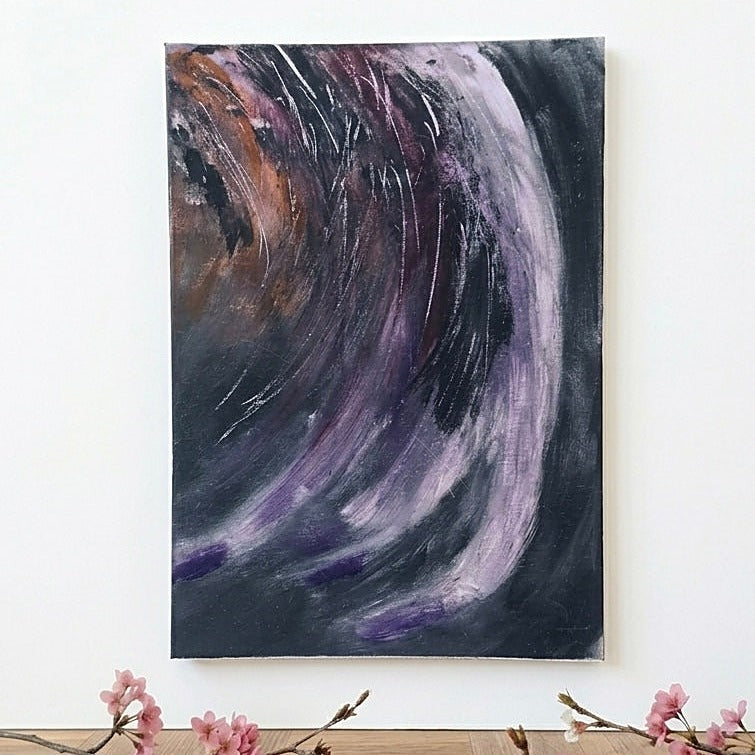 An abstract emotional drawing canvas art print painting featuring sweeping brushstrokes of purple, black, and brown, hanging on a white wall above a wooden surface with pink blossoms.