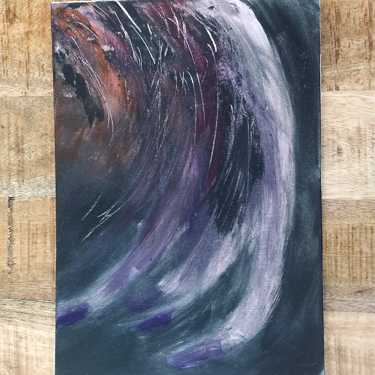 An abstract expressionist emotional drawing canvas art print painting featuring dynamic, swirling brushstrokes in purple, white, black, and brown, presented on a light wood background.