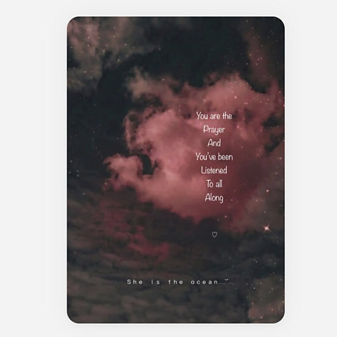 A rectangular art print greeting card with rounded corners featuring a dark cosmic nebula background in black and dusty pink, with white quote reading 'You are the Prayer And You've Been Listened To All Along' and 'She is the ocean' at the bottom.